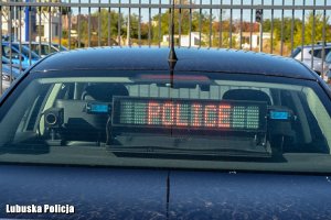 napis policja na tylnej szybie radiowozu, w tle brama i inne pojazdy