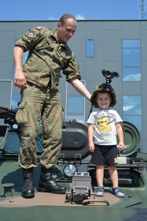 Dziecko stoi na transporterze rozpoznawczym TRI z hełmem na głowie, obok stoi żołnierz
