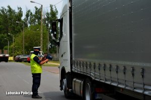 policjant stojąc przy ciężarówce patrzy w ekran miernika prędkości