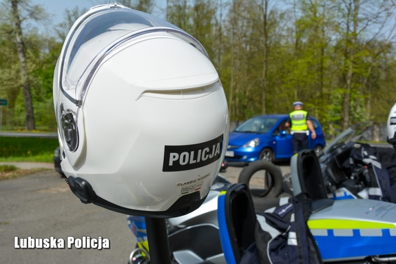Napis Policja na kasku motocyklowym, w tle policjant rozmawia z kierowcą